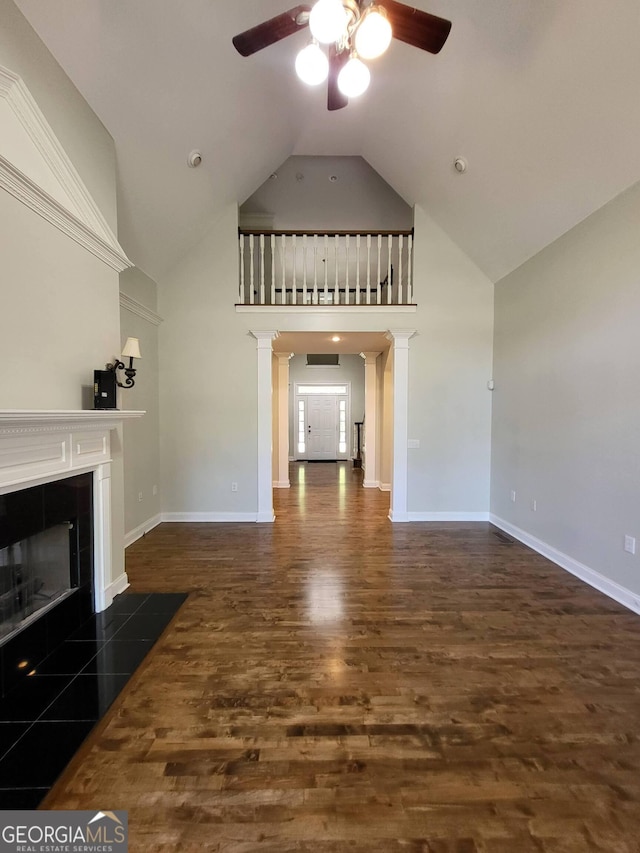 unfurnished living room featuring baseboards, ceiling fan, dark wood-type flooring, ornate columns, and a fireplace