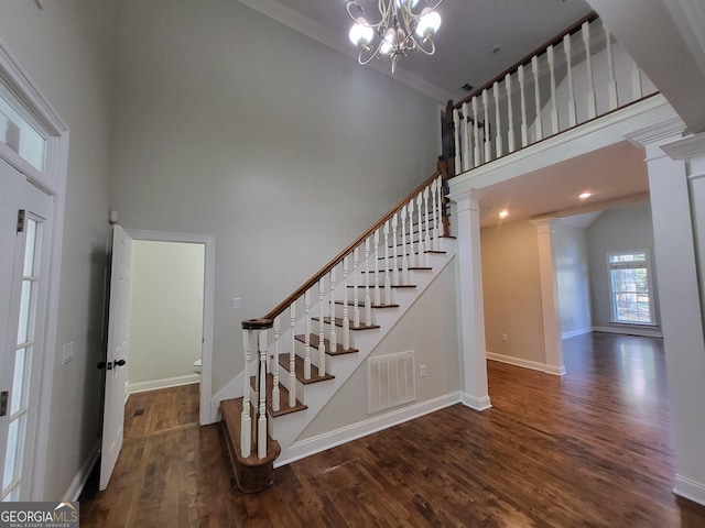 staircase with ornate columns, visible vents, a towering ceiling, wood finished floors, and baseboards