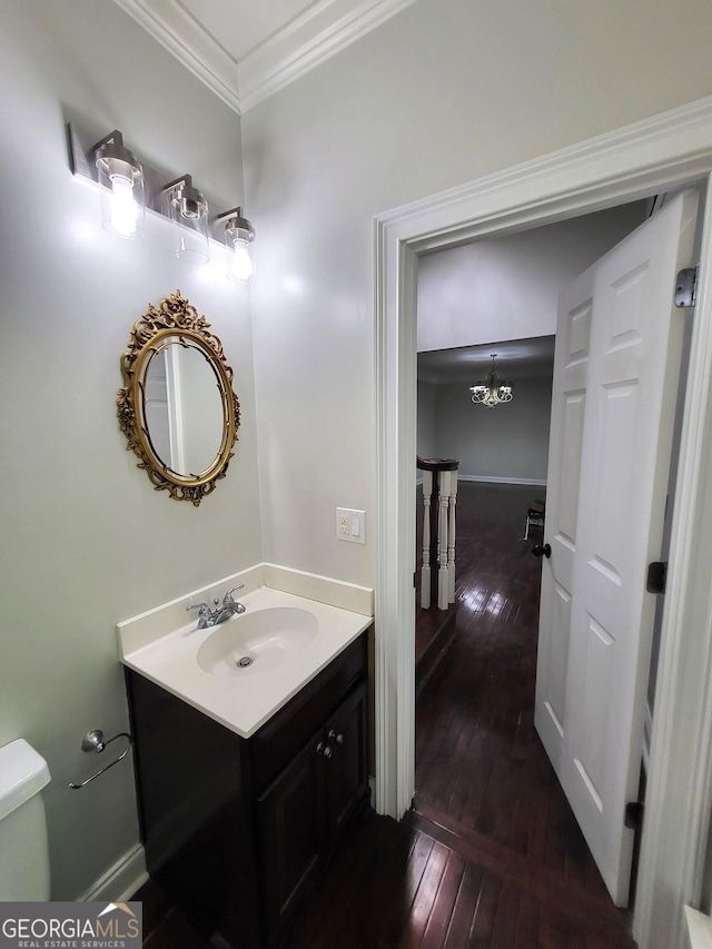 bathroom with toilet, wood finished floors, vanity, baseboards, and crown molding