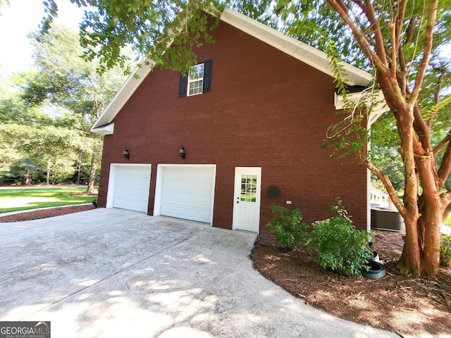 view of home's exterior with brick siding, driveway, an attached garage, and central air condition unit