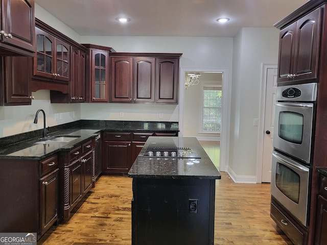 kitchen featuring black electric stovetop, light wood-style flooring, a sink, a center island, and glass insert cabinets