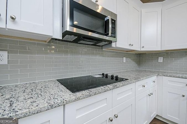 kitchen featuring tasteful backsplash, black electric cooktop, white cabinetry, and light stone counters