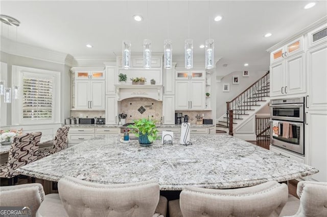 kitchen featuring ornamental molding, decorative light fixtures, a center island with sink, and white cabinets