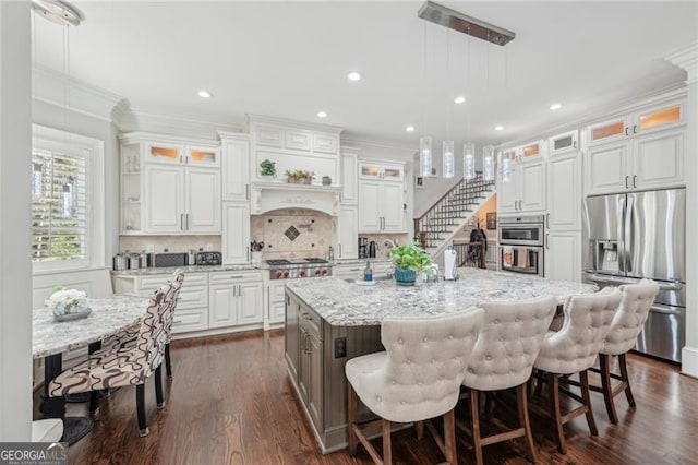 kitchen featuring appliances with stainless steel finishes, pendant lighting, white cabinets, and an island with sink