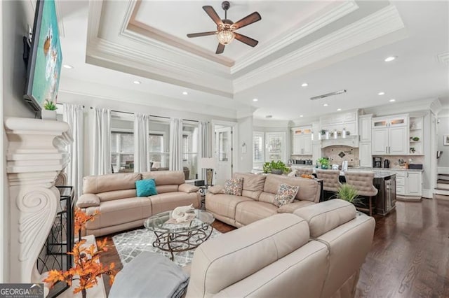 living area featuring a fireplace, a raised ceiling, dark wood finished floors, and crown molding