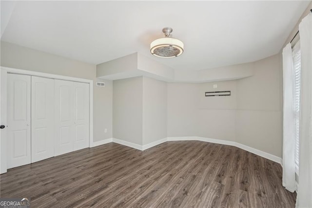 unfurnished bedroom with dark wood-style floors, a closet, visible vents, and baseboards