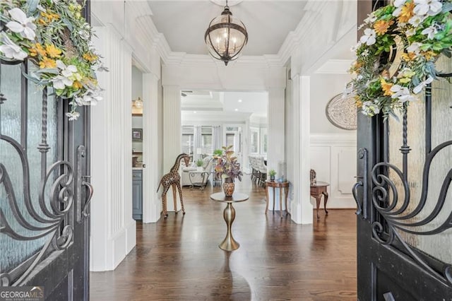 foyer with an inviting chandelier, dark wood-style flooring, a decorative wall, and crown molding