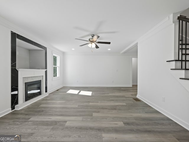 unfurnished living room featuring hardwood / wood-style flooring, ceiling fan, a premium fireplace, and ornamental molding