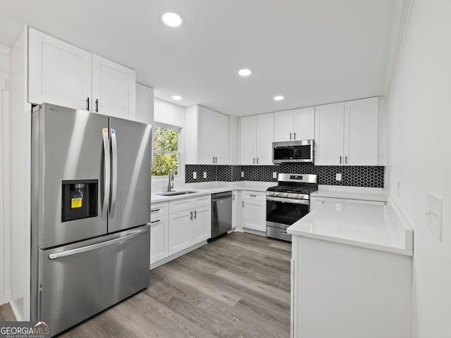 kitchen featuring appliances with stainless steel finishes, light wood-type flooring, tasteful backsplash, sink, and white cabinetry