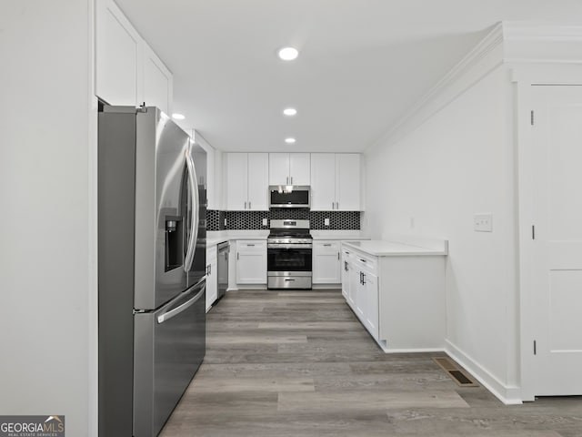 kitchen with appliances with stainless steel finishes, light hardwood / wood-style flooring, white cabinetry, and tasteful backsplash