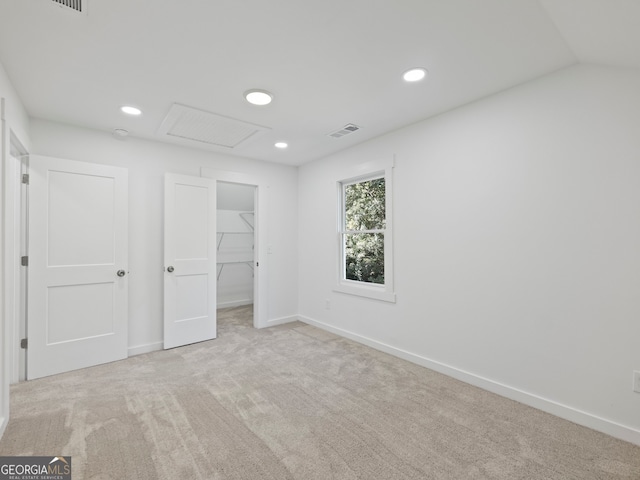 unfurnished bedroom with lofted ceiling, a walk in closet, light carpet, and a closet