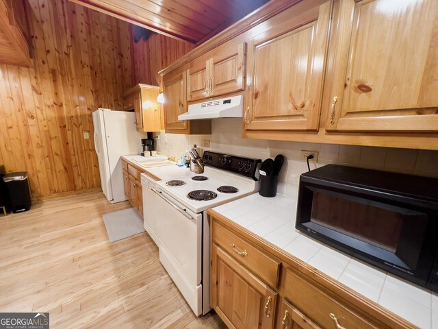 kitchen with sink, light hardwood / wood-style floors, tile counters, wooden walls, and white appliances