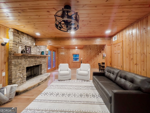 living room with wood ceiling, wood walls, a stone fireplace, and hardwood / wood-style floors