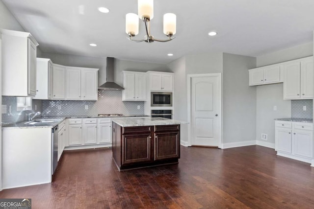 kitchen featuring wall chimney exhaust hood, white cabinetry, a chandelier, appliances with stainless steel finishes, and a kitchen island