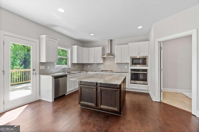 kitchen featuring white cabinets, stainless steel appliances, a center island, and wall chimney range hood