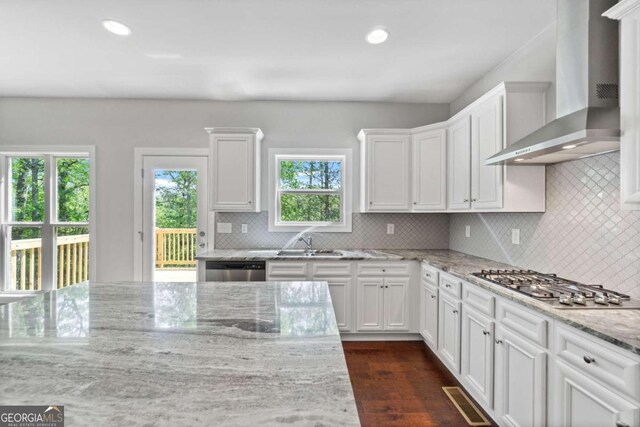 kitchen with wall chimney exhaust hood, sink, white cabinetry, appliances with stainless steel finishes, and light stone countertops