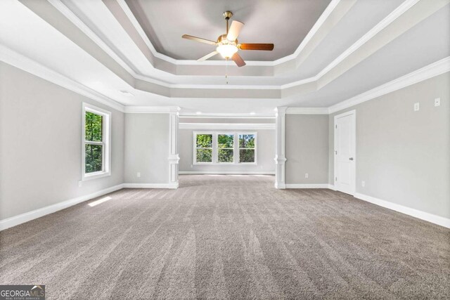 unfurnished living room featuring ornate columns, carpet, ceiling fan, a tray ceiling, and crown molding