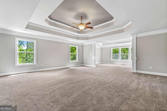 carpeted empty room with a raised ceiling, crown molding, ceiling fan, and ornate columns