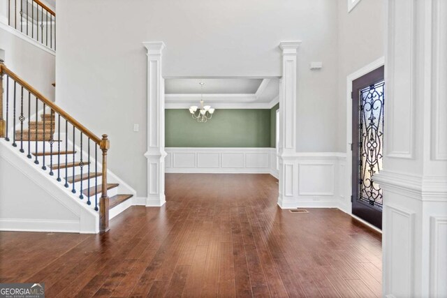 entrance foyer with dark hardwood / wood-style floors, decorative columns, and a notable chandelier