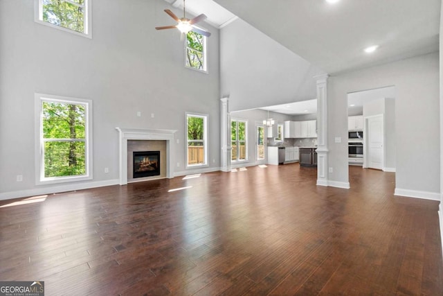 unfurnished living room featuring ceiling fan with notable chandelier, a fireplace, high vaulted ceiling, and dark wood-type flooring