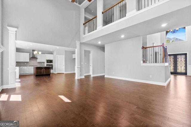 unfurnished living room featuring french doors, dark wood-type flooring, decorative columns, and a high ceiling