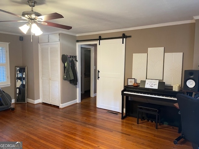 misc room with crown molding, a barn door, wood-type flooring, and ceiling fan