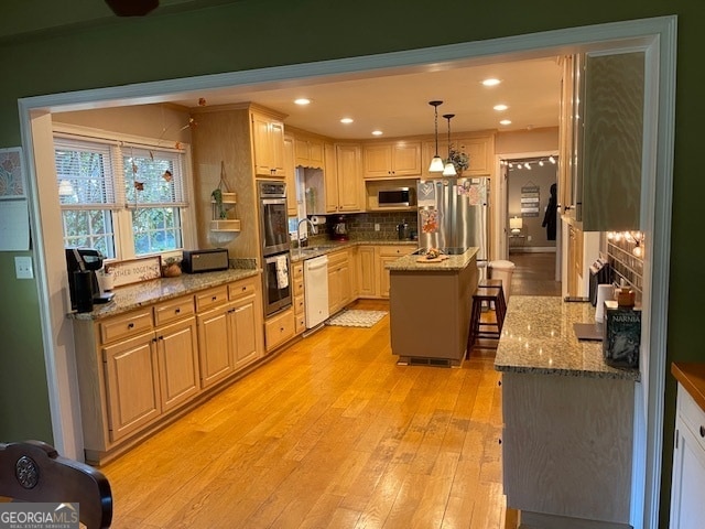 kitchen with light stone counters, appliances with stainless steel finishes, a center island, light hardwood / wood-style floors, and decorative light fixtures