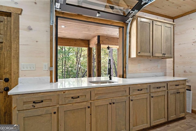 kitchen with light wood-type flooring, sink, and wooden walls