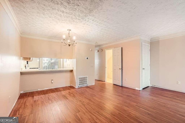 unfurnished room with a notable chandelier, ornamental molding, hardwood / wood-style flooring, and a textured ceiling