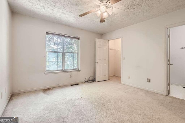 unfurnished bedroom with a closet, a spacious closet, light colored carpet, a textured ceiling, and ceiling fan