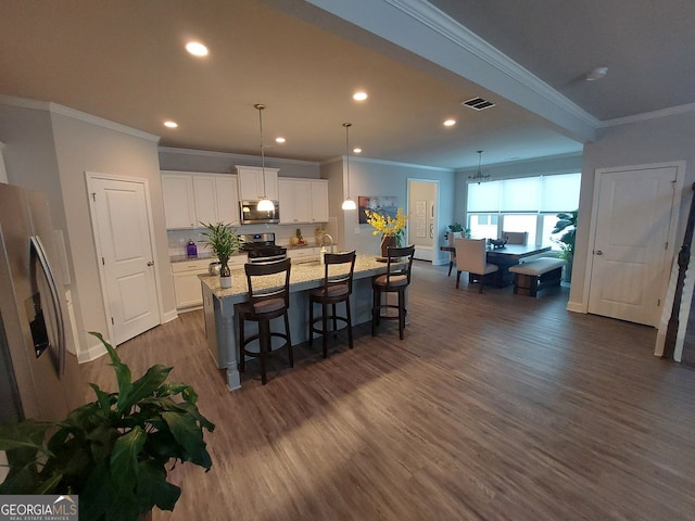 kitchen featuring appliances with stainless steel finishes, dark hardwood / wood-style flooring, white cabinets, ornamental molding, and a center island with sink