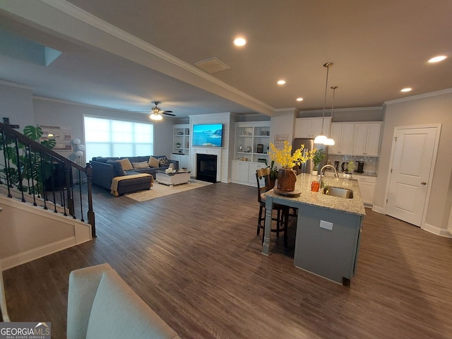 kitchen with dark wood-type flooring, an island with sink, sink, pendant lighting, and white cabinetry