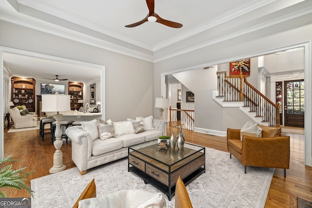 living room with crown molding, hardwood / wood-style flooring, a tray ceiling, and ceiling fan