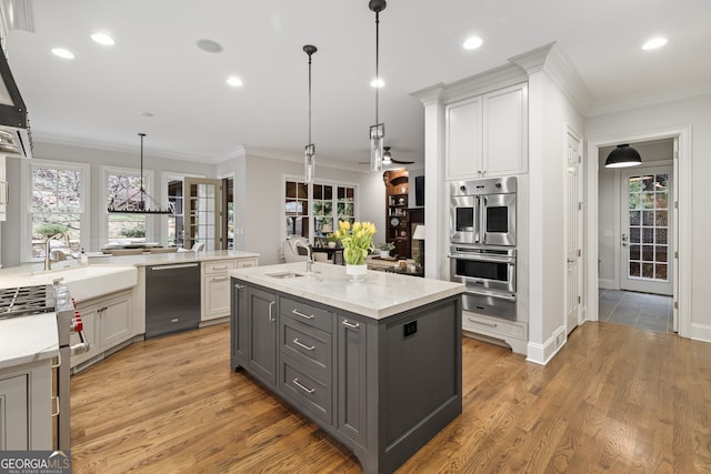 kitchen with white cabinets, an island with sink, appliances with stainless steel finishes, gray cabinetry, and light hardwood / wood-style floors