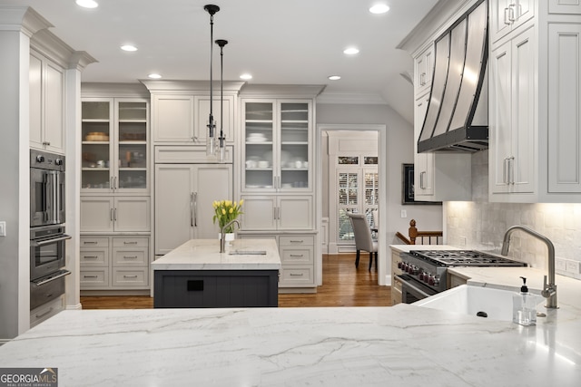 kitchen featuring premium appliances, hanging light fixtures, crown molding, decorative backsplash, and a center island with sink