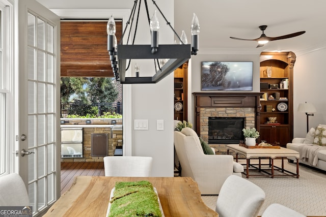 living room with a stone fireplace, built in features, ceiling fan, crown molding, and hardwood / wood-style flooring