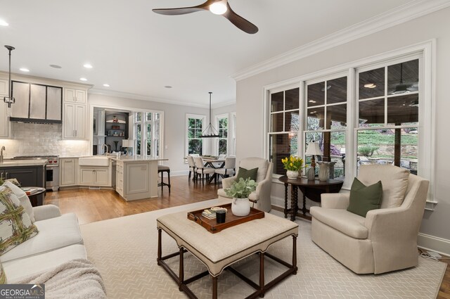 living room featuring a wealth of natural light, ornamental molding, sink, and light wood-type flooring