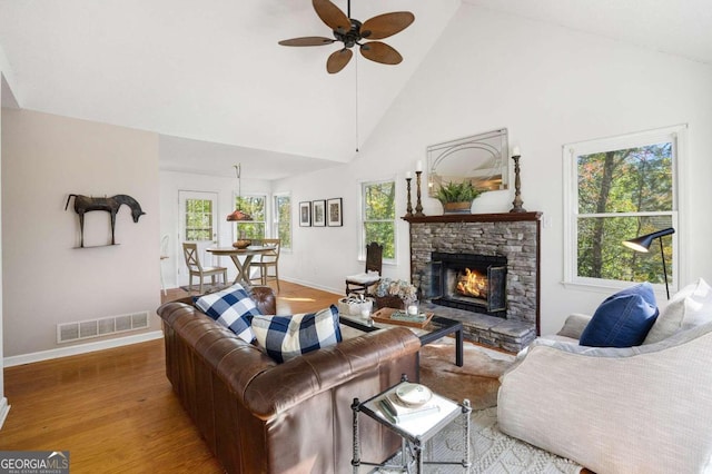 living room featuring light hardwood / wood-style flooring, a stone fireplace, high vaulted ceiling, and ceiling fan