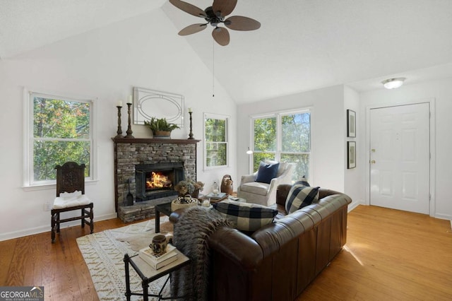 living room featuring high vaulted ceiling, a stone fireplace, wood-type flooring, and ceiling fan