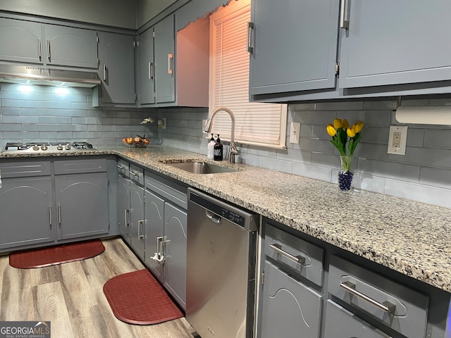 kitchen featuring light hardwood / wood-style floors, sink, backsplash, light stone countertops, and appliances with stainless steel finishes