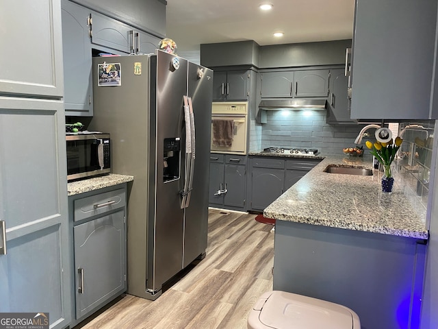 kitchen with stainless steel appliances, backsplash, stone counters, sink, and light hardwood / wood-style floors