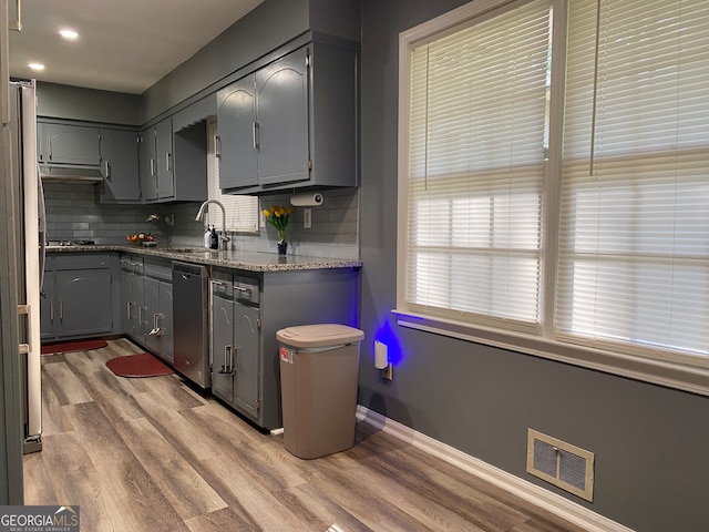 kitchen featuring decorative backsplash, stainless steel dishwasher, hardwood / wood-style floors, and gray cabinetry