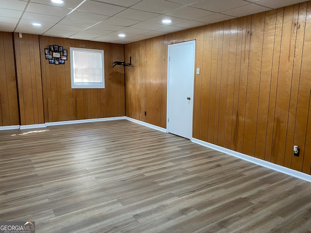 unfurnished room featuring a drop ceiling, wood-type flooring, and wooden walls