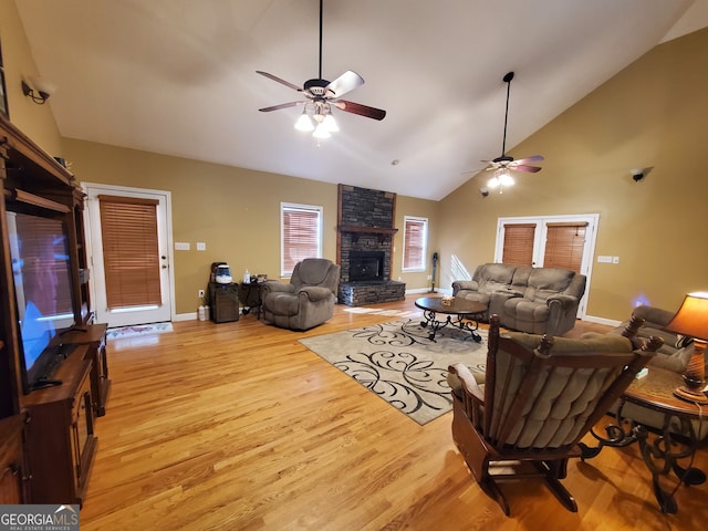 living room with ceiling fan, a stone fireplace, high vaulted ceiling, and light wood-type flooring