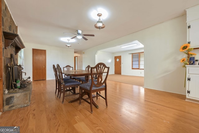 dining area with a stone fireplace, light wood-type flooring, and ceiling fan