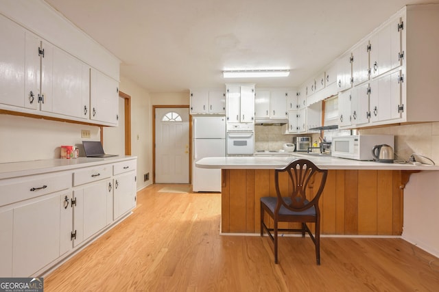 kitchen featuring white appliances, tasteful backsplash, light wood-type flooring, a kitchen bar, and white cabinetry