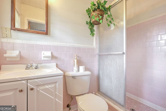 bathroom with tile walls, vanity, a shower with shower door, and toilet