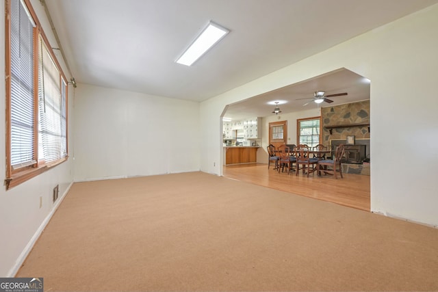 unfurnished living room with light hardwood / wood-style flooring, ceiling fan, a wood stove, and a wealth of natural light