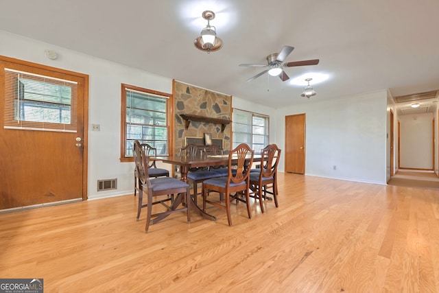 dining area with a stone fireplace, ceiling fan, light hardwood / wood-style floors, and plenty of natural light