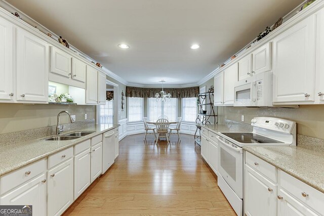 kitchen featuring white cabinets, light wood-type flooring, a notable chandelier, white appliances, and ornamental molding